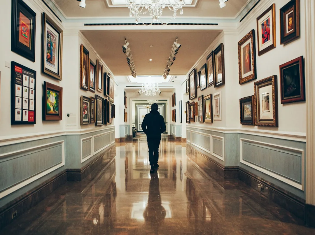 Art gallery hallway with framed paintings on both walls and polished marble floor with silhouette of person walking