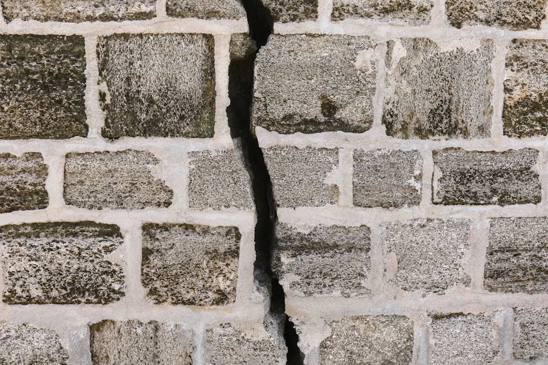 Large structural crack running vertically through stone brick wall indicating serious load-bearing wall failure