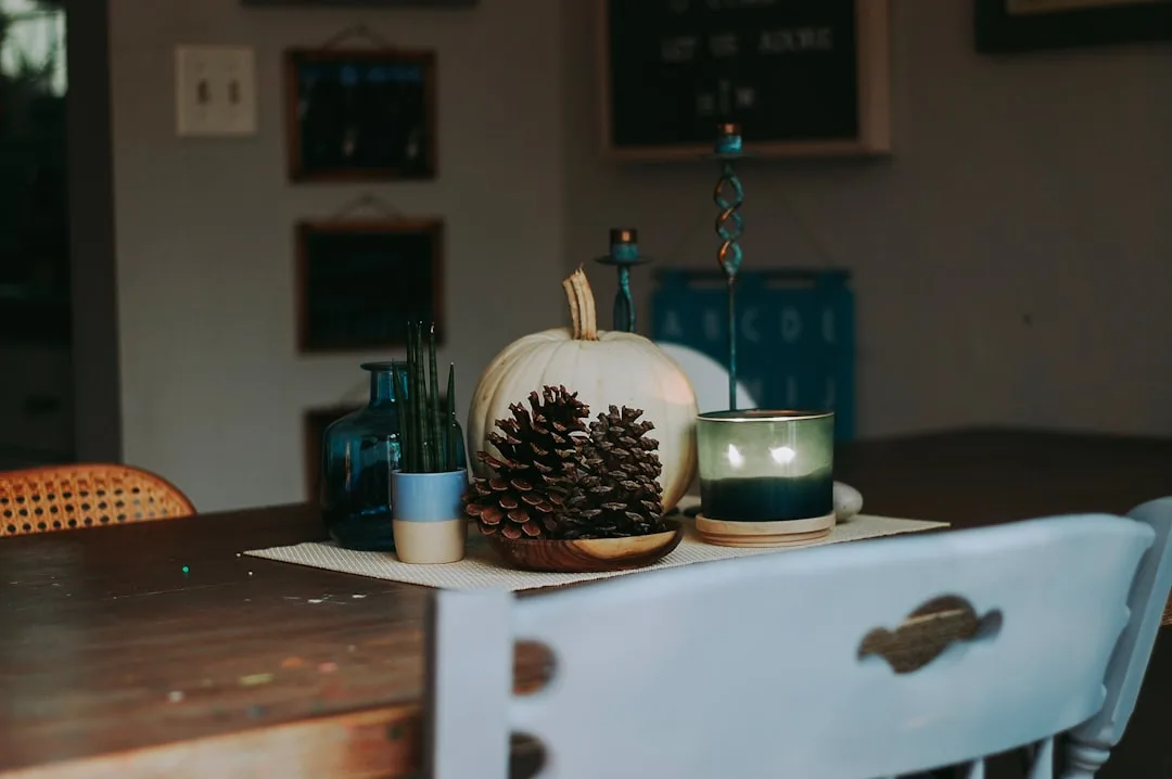White pumpkin, pine cones, and green candle fall centerpiece on wooden dining table for autumn decor