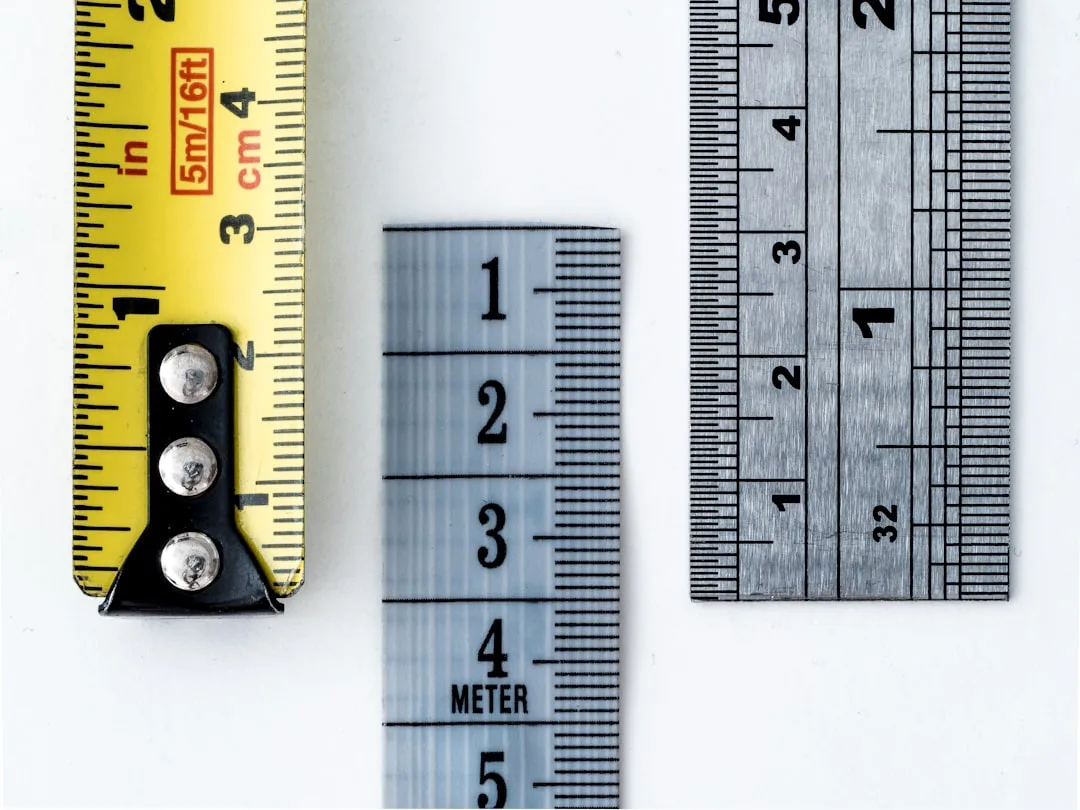 Yellow tape measure, fabric measuring tape, and metal ruler side by side showing measurement markings in inches and cent