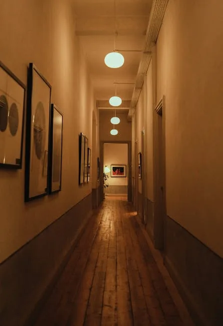 Long hallway with framed artwork gallery wall, warm pendant lights, and rustic hardwood floors