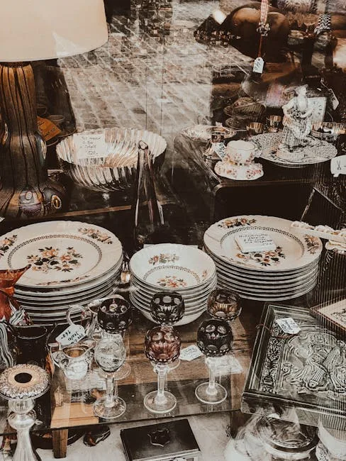 Antique shop display with stacked floral china plates, crystal wine glasses, and vintage decorative pieces for farmhouse