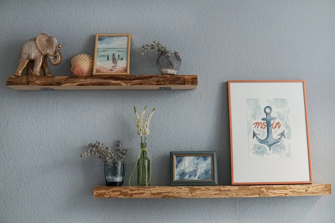 Two rustic wooden floating shelves styled with elephant figurine, seashell, framed art, vases, and anchor print on gray 