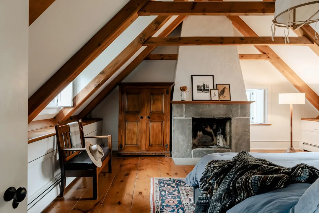 Boho farmhouse attic bedroom with exposed wood beams, stone fireplace, Persian rug, and layered textiles