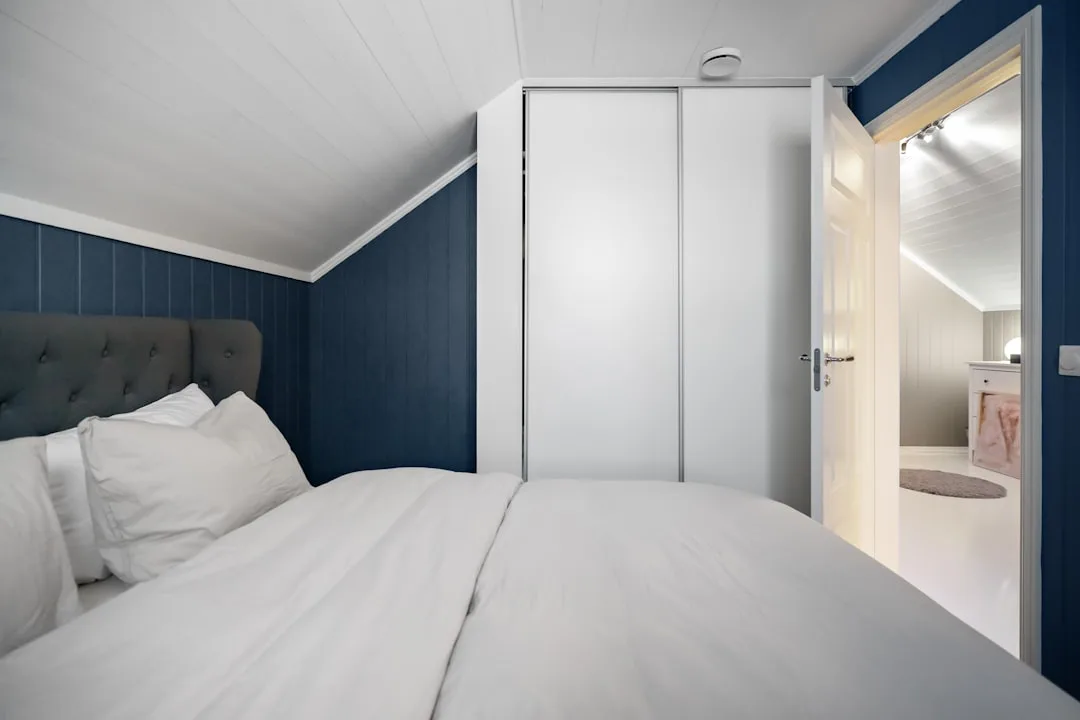 Attic bedroom conversion with sloped ceiling, built-in white wardrobe, dark blue walls, and white bedding