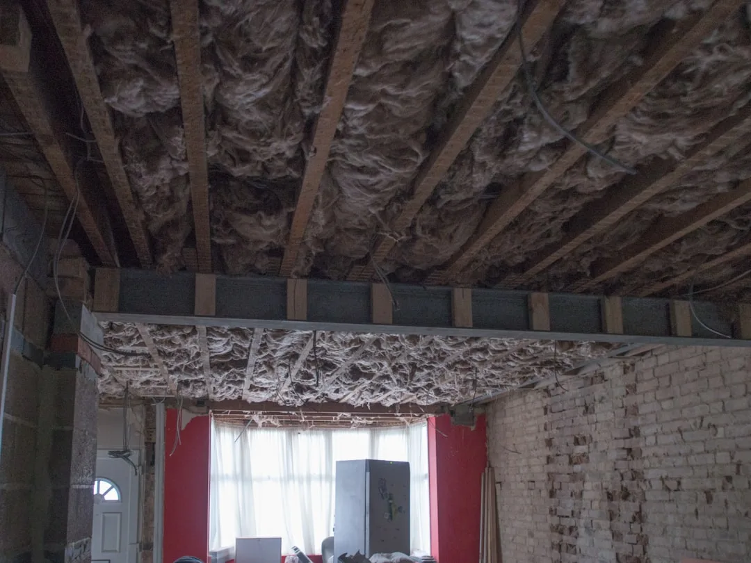 Exposed roof joists with fiberglass batt insulation visible between rafters during attic conversion renovation
