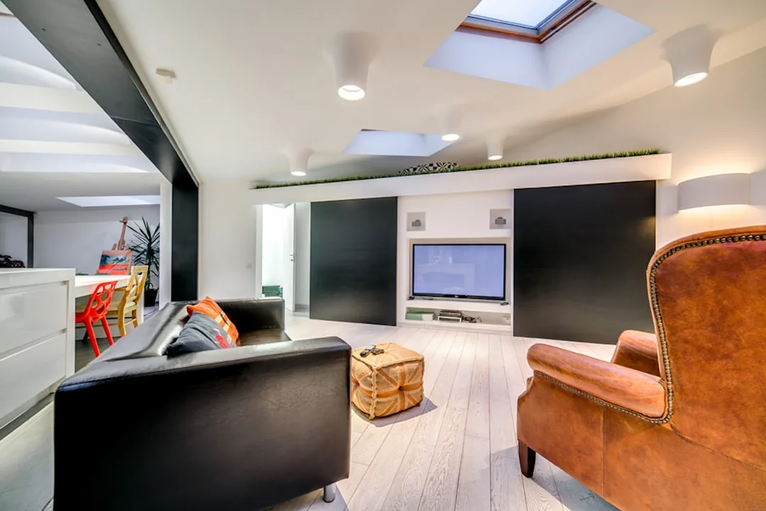 Converted attic living room with skylights, white ceiling, hardwood floor, black panels and leather seating