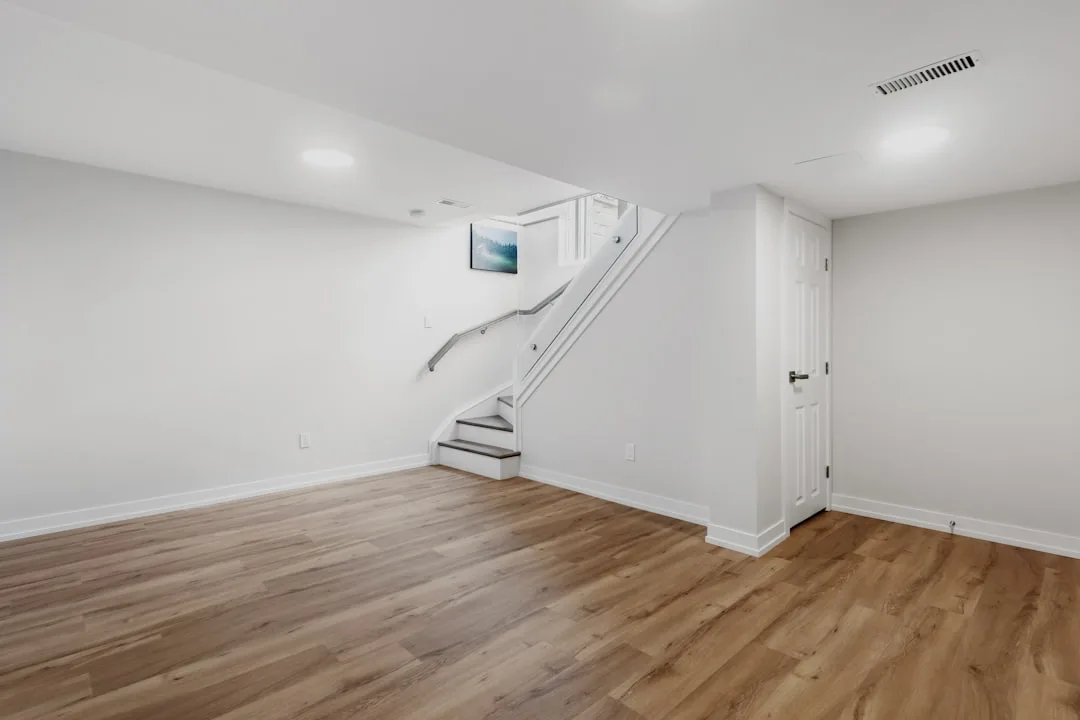 Interior basement entryway with white staircase, hardwood floors, and door in finished basement space
