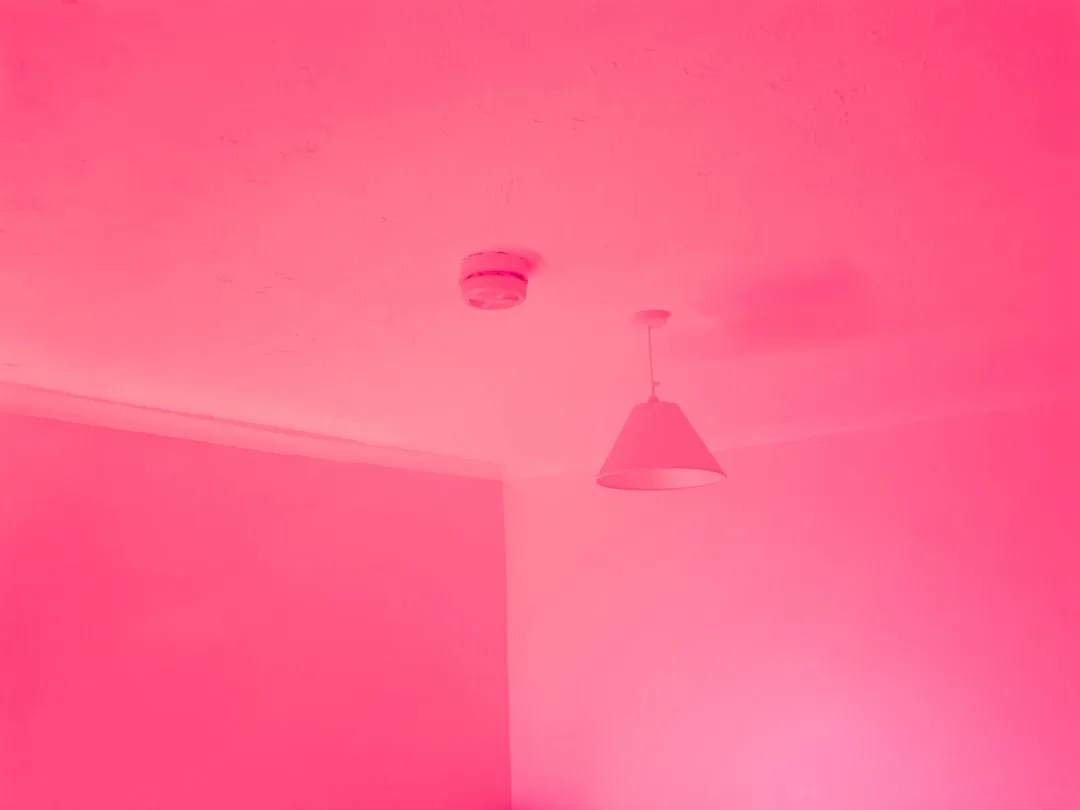 Room interior bathed in intense pink light showing ceiling, pendant lamp and walls in vivid magenta hue
