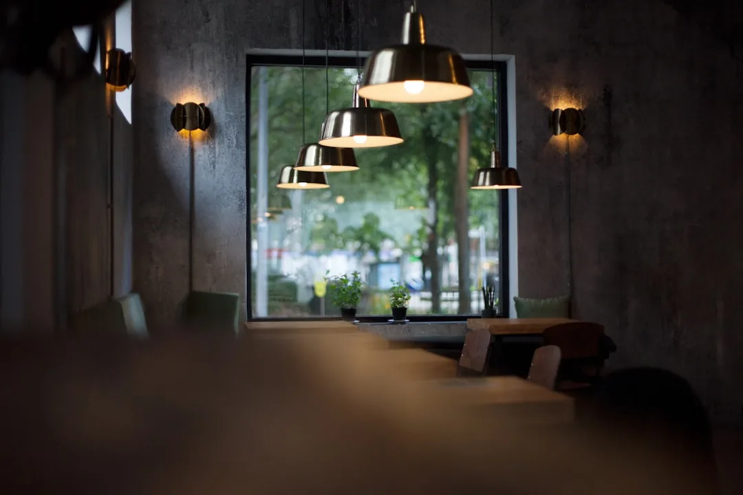 Layered restaurant lighting with pendant metal lamps and wall sconces creating ambient atmosphere near large window