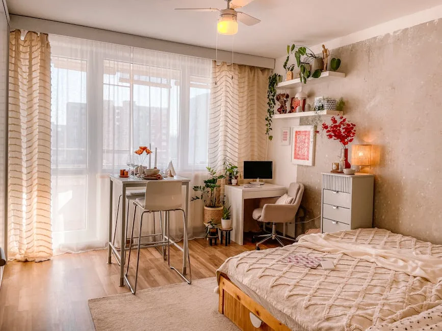 Layered small studio apartment with sheer curtains, desk workspace, wall shelves with plants, and cozy bed styling
