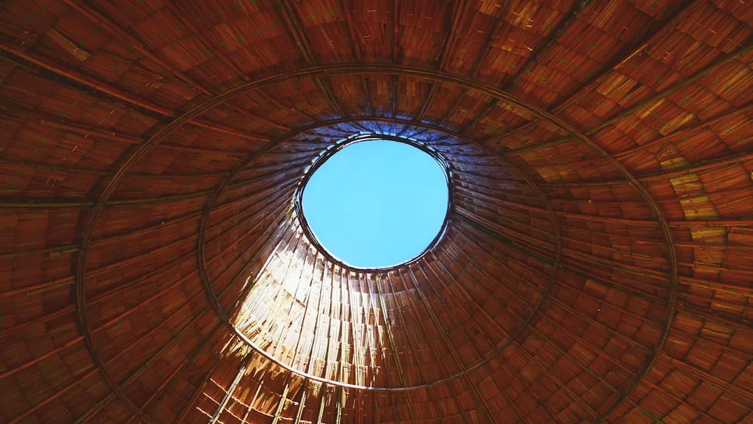 Upward view through circular bamboo roof opening revealing blue sky, demonstrating natural light and airflow design stra