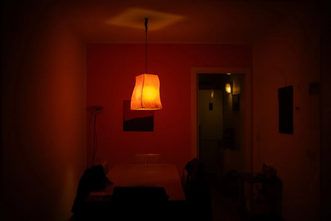 Warm orange pendant lamp illuminating a dimly lit red-walled room showing dramatic lighting effect on wall colors