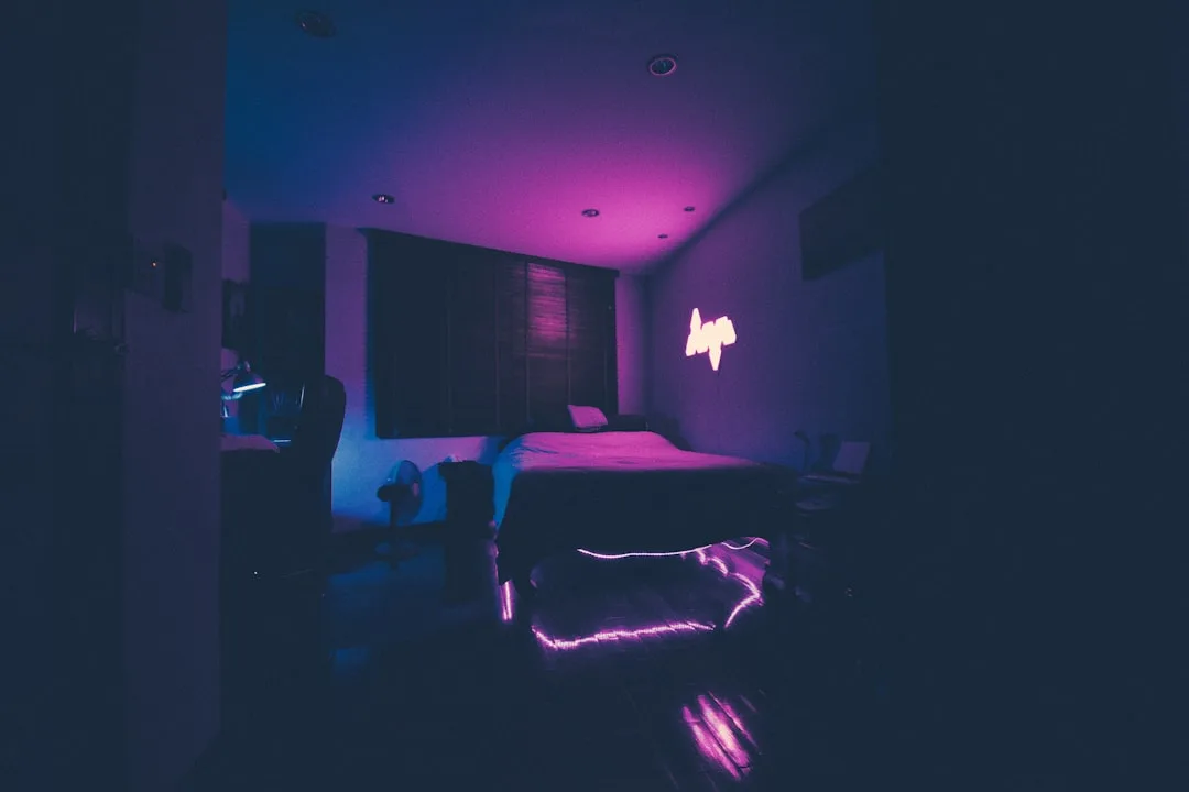 Dark dorm bedroom lit by purple neon 'hope' sign and pink LED strip lights creating moody ambient lighting