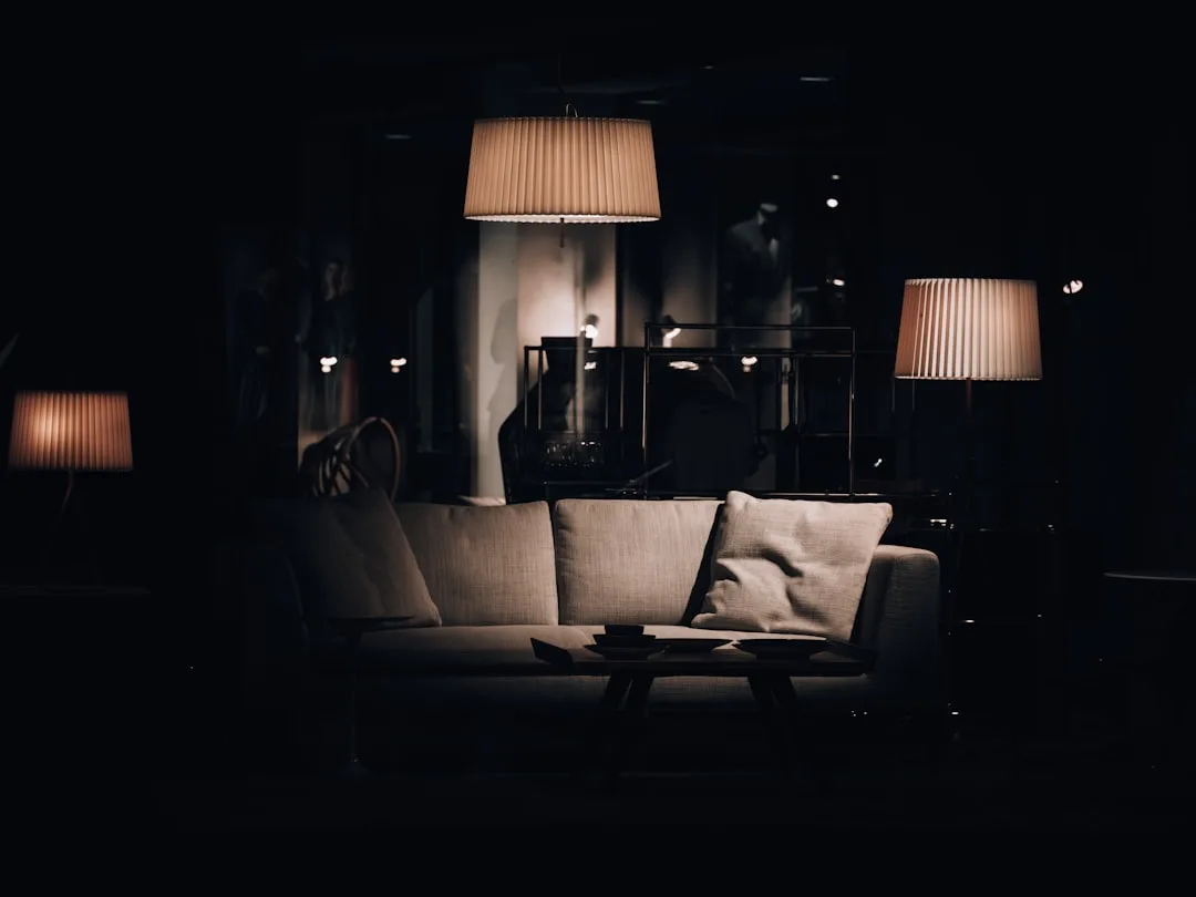 Dramatic moody living room with pendant lamp and floor lamps illuminating a neutral sofa in near darkness