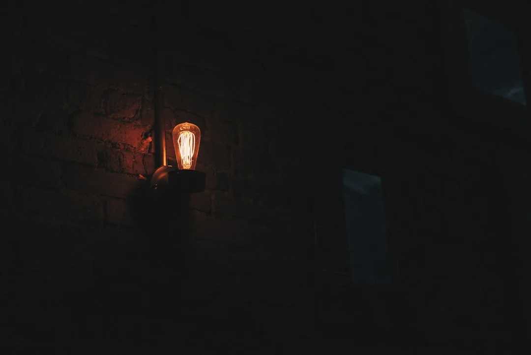 Vintage Edison bulb wall sconce glowing against dark brick wall creating dramatic moody atmosphere