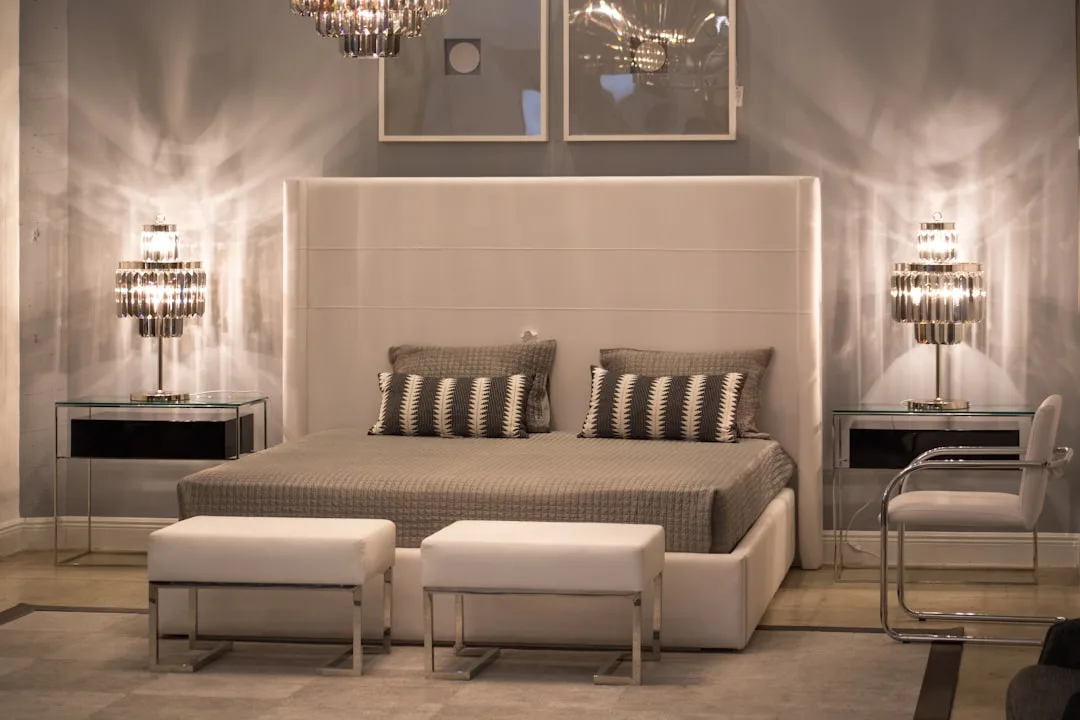 Luxury bedroom with crystal wall sconces casting dramatic light patterns on walls beside white upholstered headboard