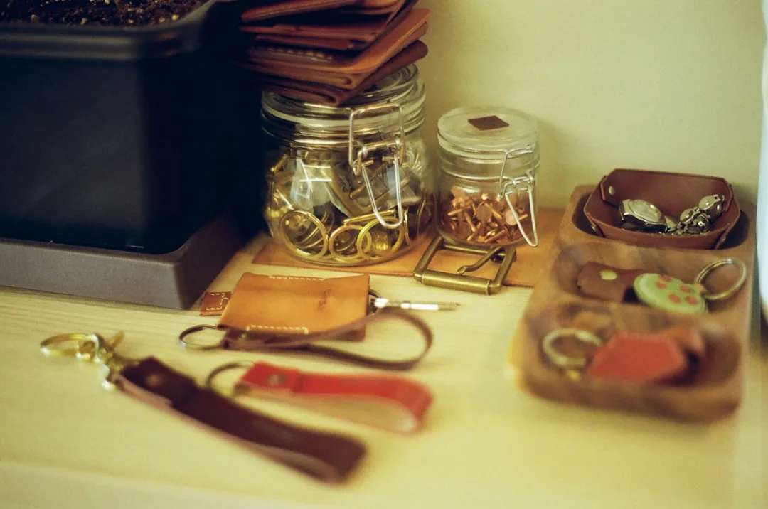 Cluttered desk with multiple small leather keychains, glass jars of hardware, and tiny accessories illustrating accessor