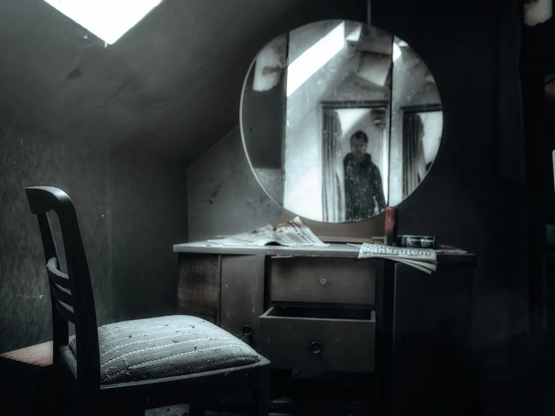 Round mirror on vintage dresser in abandoned dark room reflecting silhouette of photographer