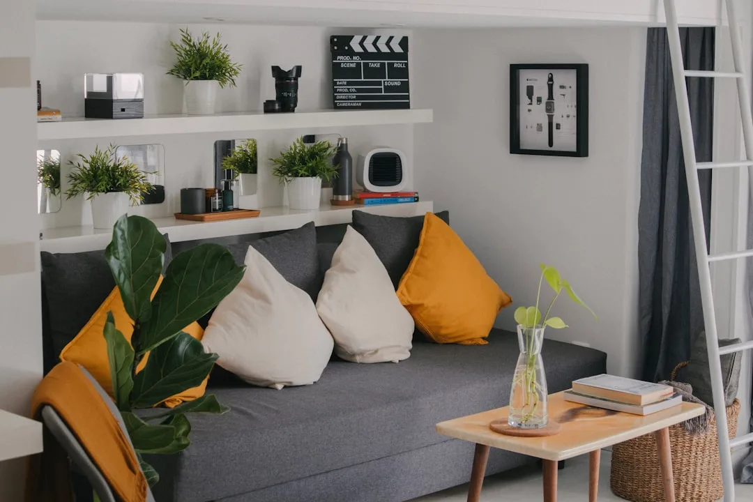 Small living room with gray sofa, yellow pillows, shelves with plants and decor, coffee table — budget decorating strate
