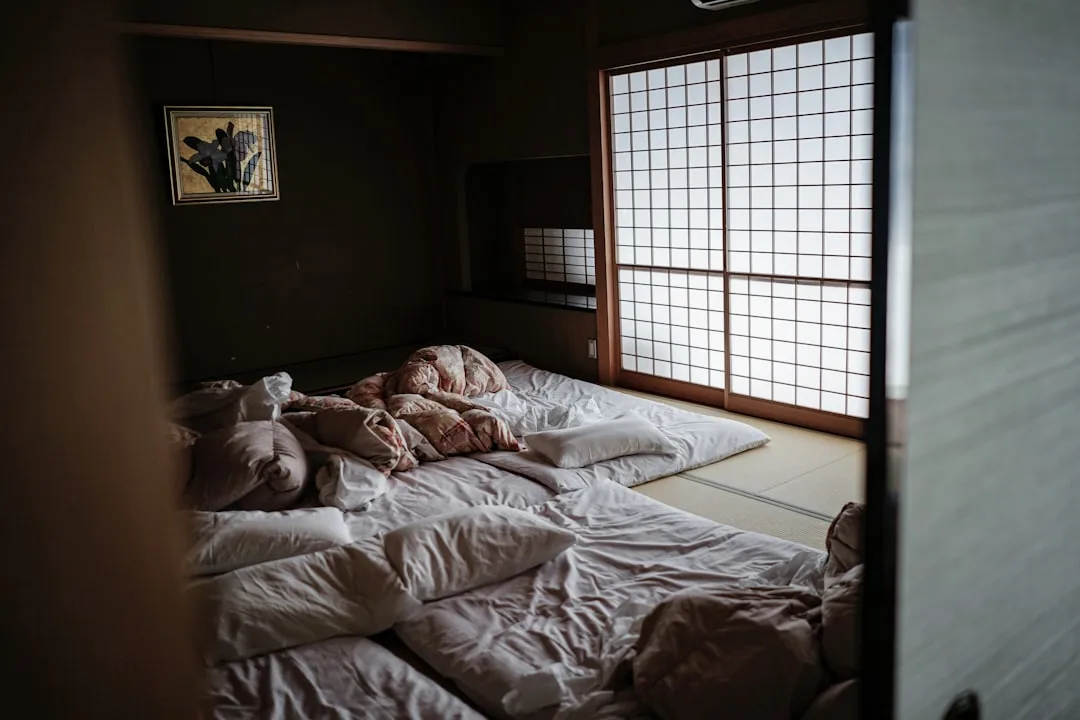Japanese futon bedding layered on tatami floor with shoji screens in a traditional Japandi bedroom