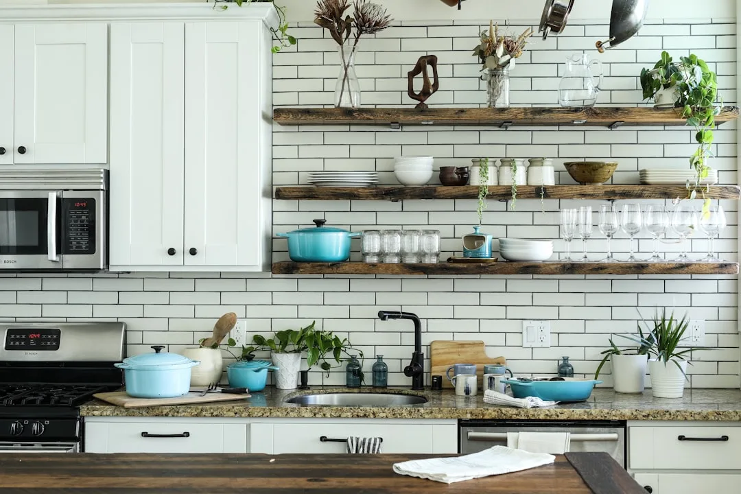 Rustic wood open kitchen shelves with teal cookware, glassware, and plants on white subway tile backsplash
