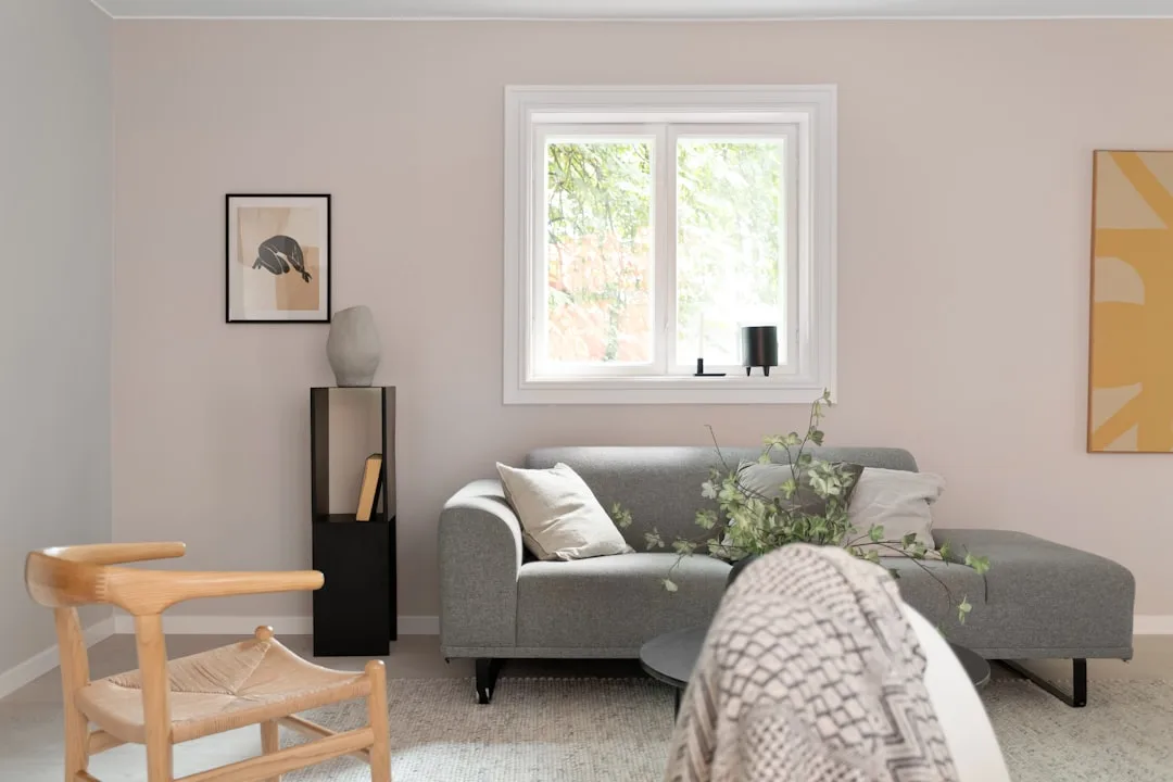 Scandinavian living room with soft blush pink walls, gray modern sectional sofa, wooden wishbone chair, and minimalist d