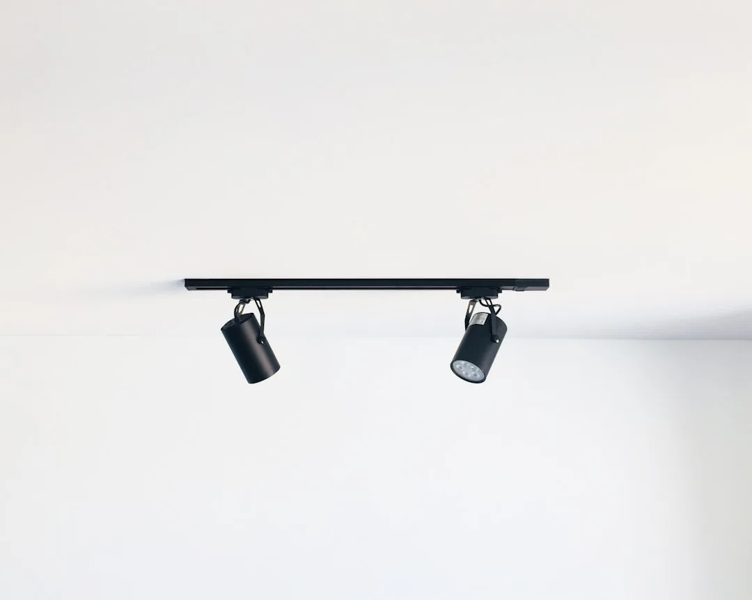 Black two-head track lighting fixture mounted on white ceiling, showing adjustable directional spotlights