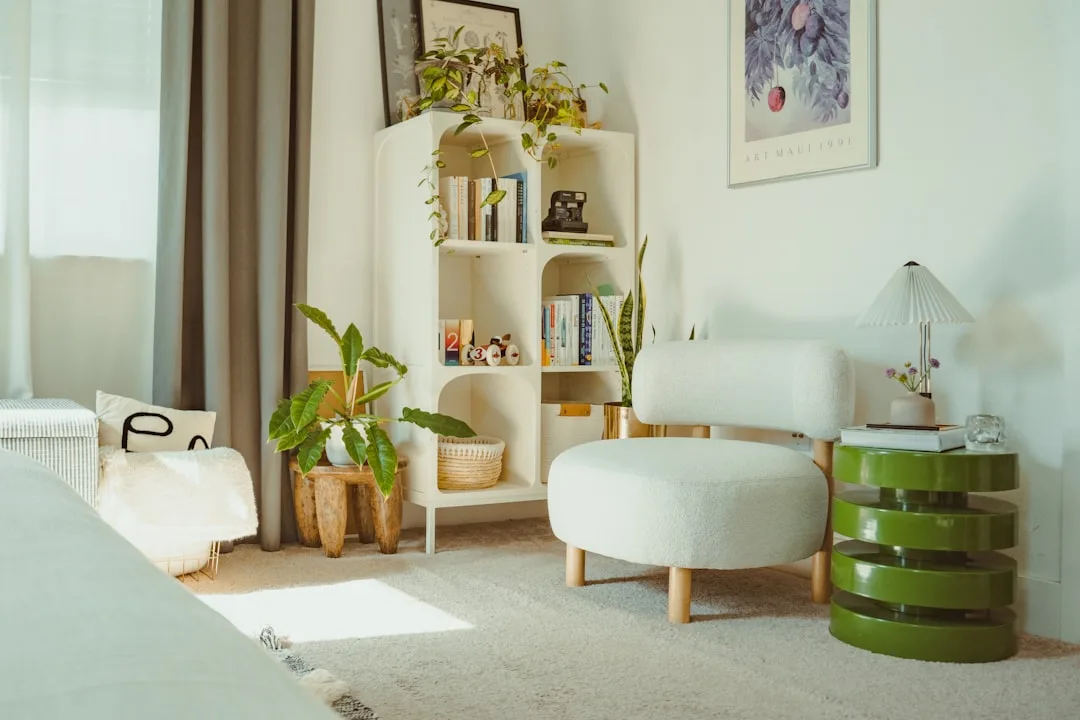 Cozy bedroom reading nook with white boucle chair, green side table lamp, white bookshelf and indoor plants