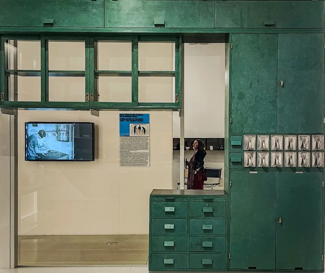 Frankfurt Kitchen museum exhibit showing green modular cabinet storage system with glass upper cabinets and drawer units