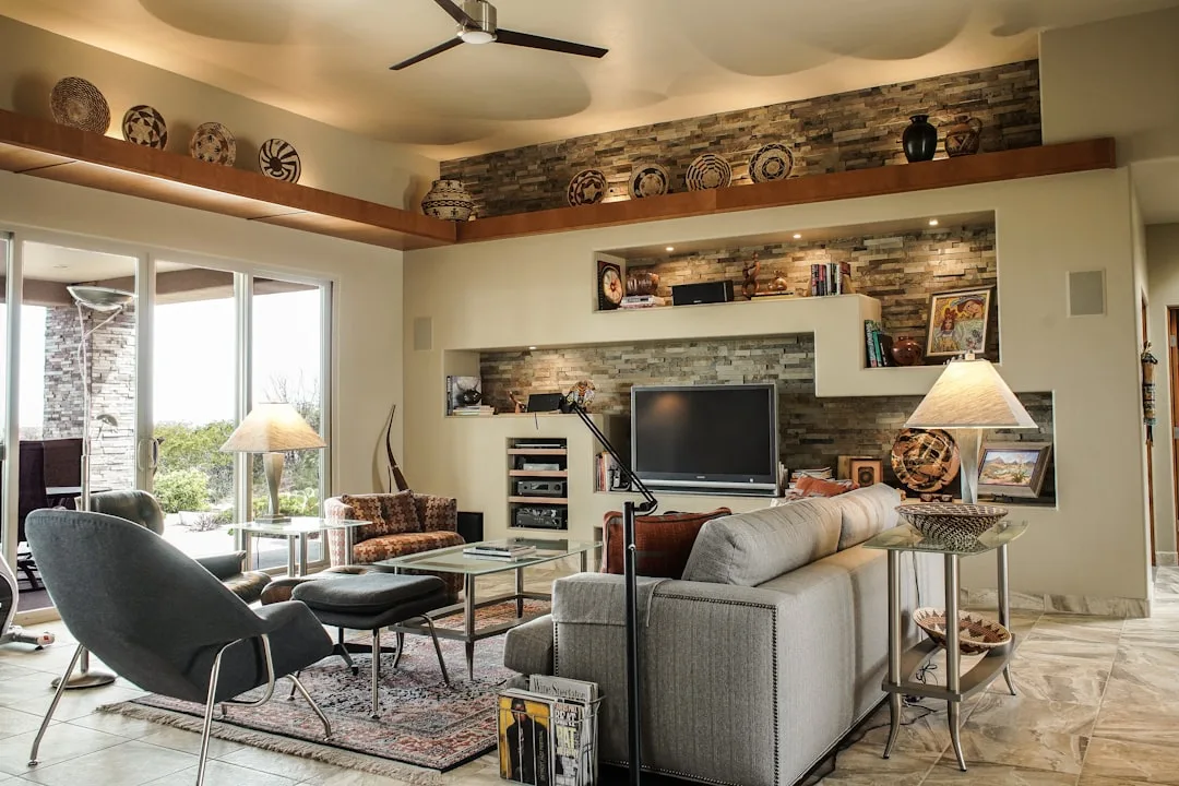 Southwestern living room with tray ceiling, recessed stone accent wall, and high-mounted decorative shelves creating ver