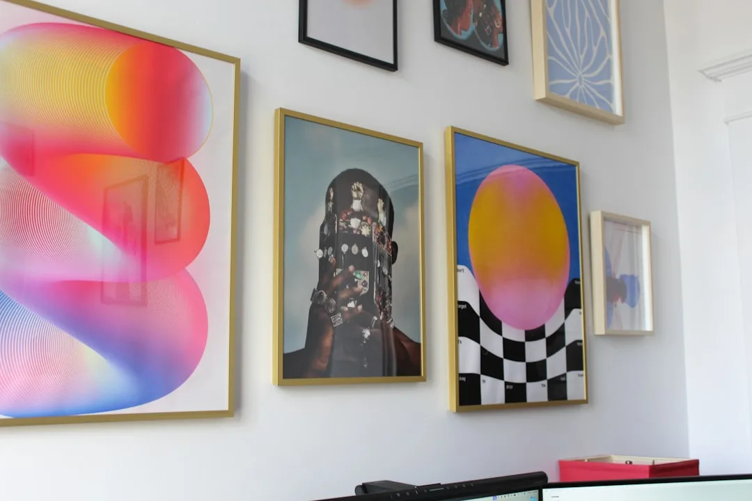 Gallery wall with colorful framed art prints including abstract and portrait artwork displayed in a home office setting