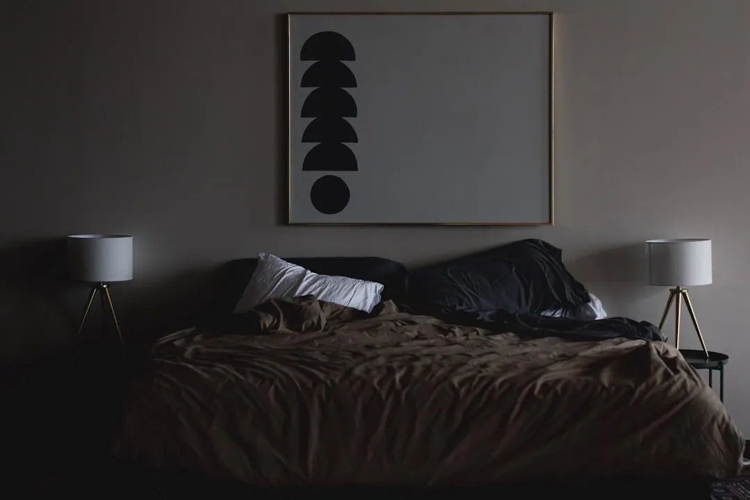 Dark moody bedroom with framed wall art and two tripod lamps on either side of an unmade bed
