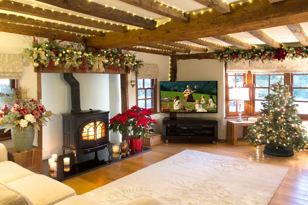 Christmas living room with fairy lights on rustic wooden ceiling beams, decorated fireplace mantel and lit Christmas tre