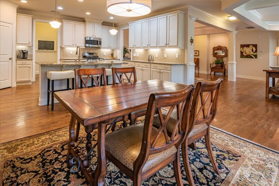 Rustic farmhouse dining room with dark wood table and chairs adjacent to white kitchen with granite island