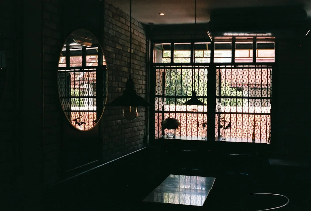 Dark industrial-style interior with brick wall, oval mirror, metal pendant light, and diamond-grid windows