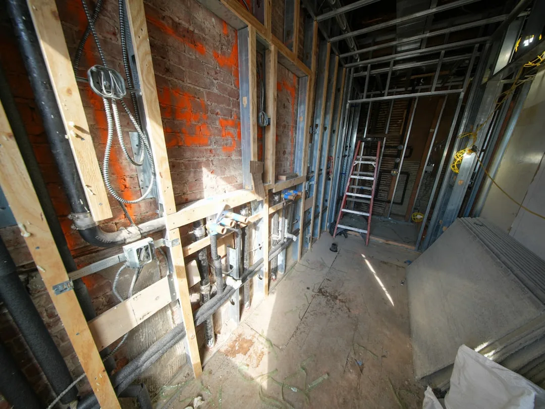 Kitchen renovation rough-in phase showing exposed framing, electrical conduit, plumbing pipes, and metal stud wall frami