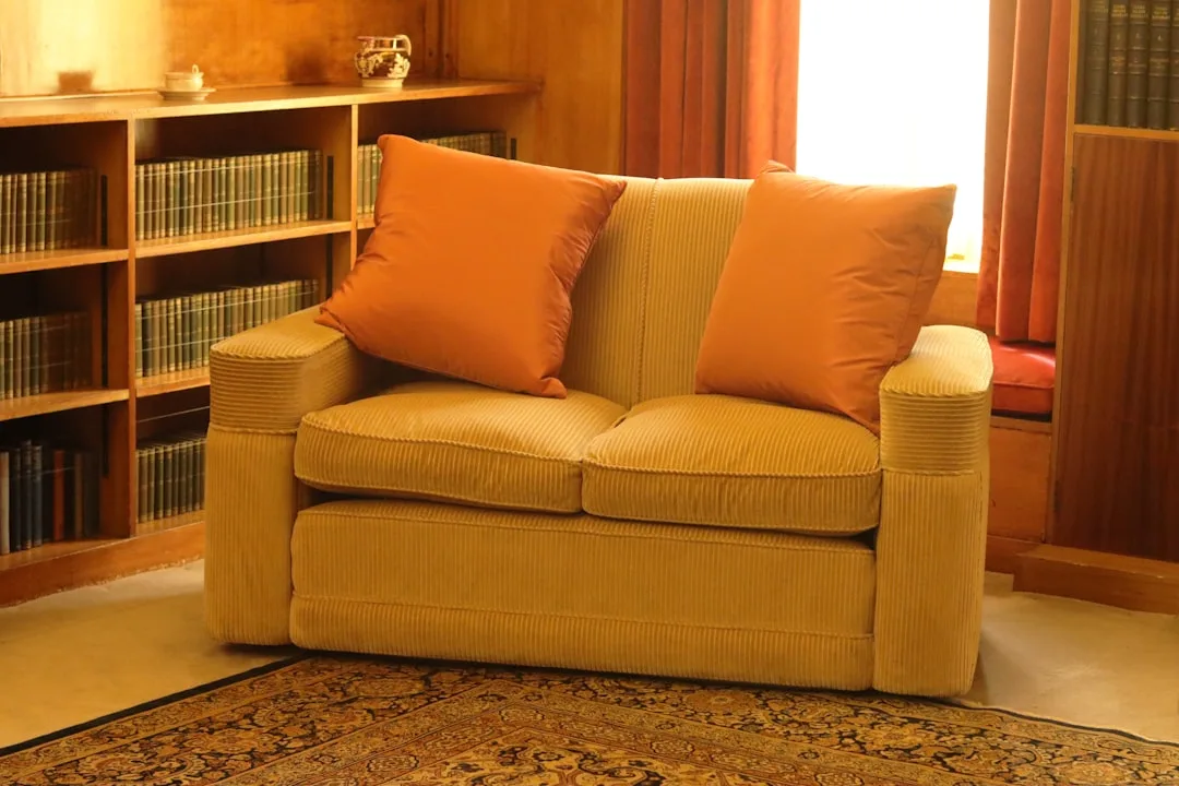 Tan corduroy loveseat with orange cushions beside bookshelf in warm library room illustrating sofa sizing proportions