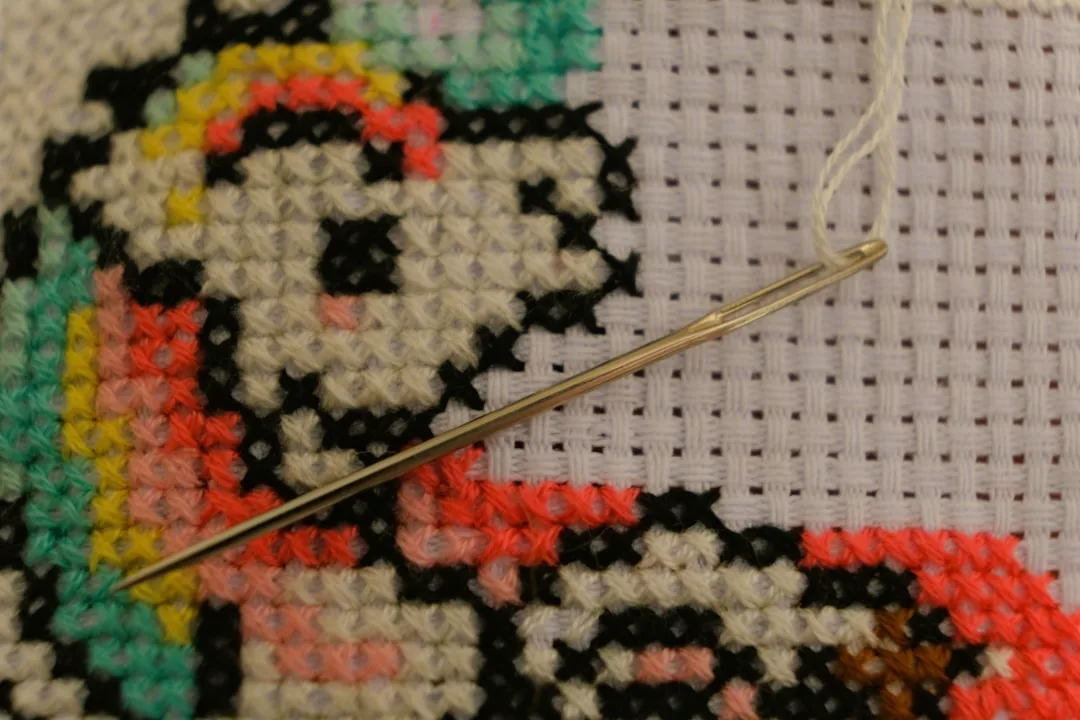 Close-up of a sewing needle on colorful cross-stitch embroidery fabric with detailed stitching pattern