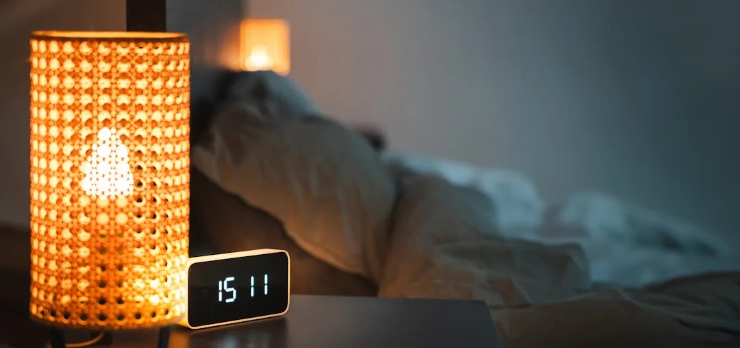 Wicker bedside lamp glowing warmly next to a digital clock showing 15:11 on a bedroom nightstand