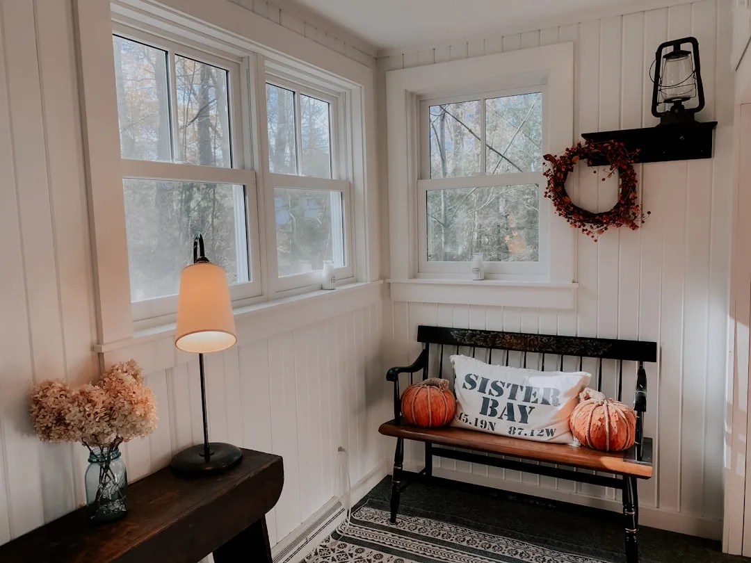 Cozy fall entryway with vintage black bench, pumpkin decor, berry wreath, and thrifted lamp in white cottage room