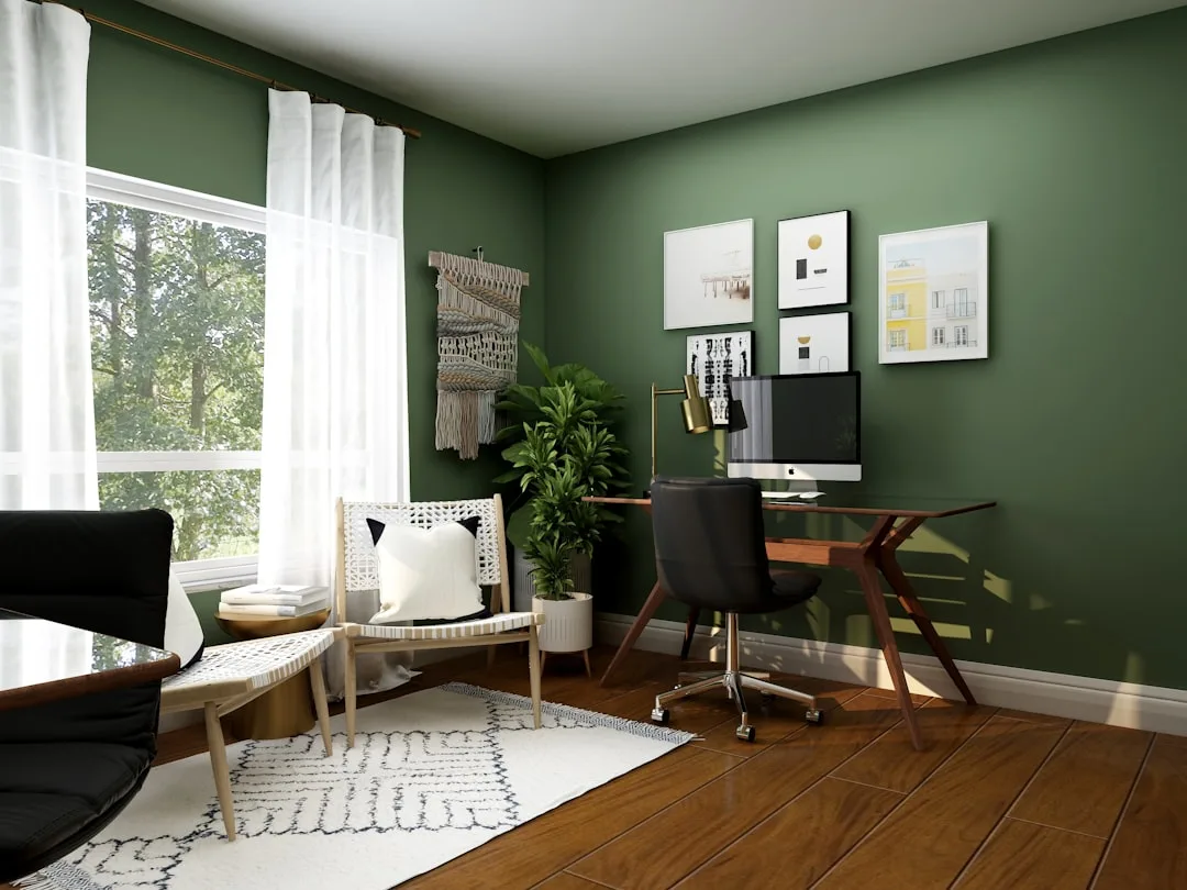 Organized home office with clear desk surface, green walls, wooden floor, and minimal decor in a modern boho style