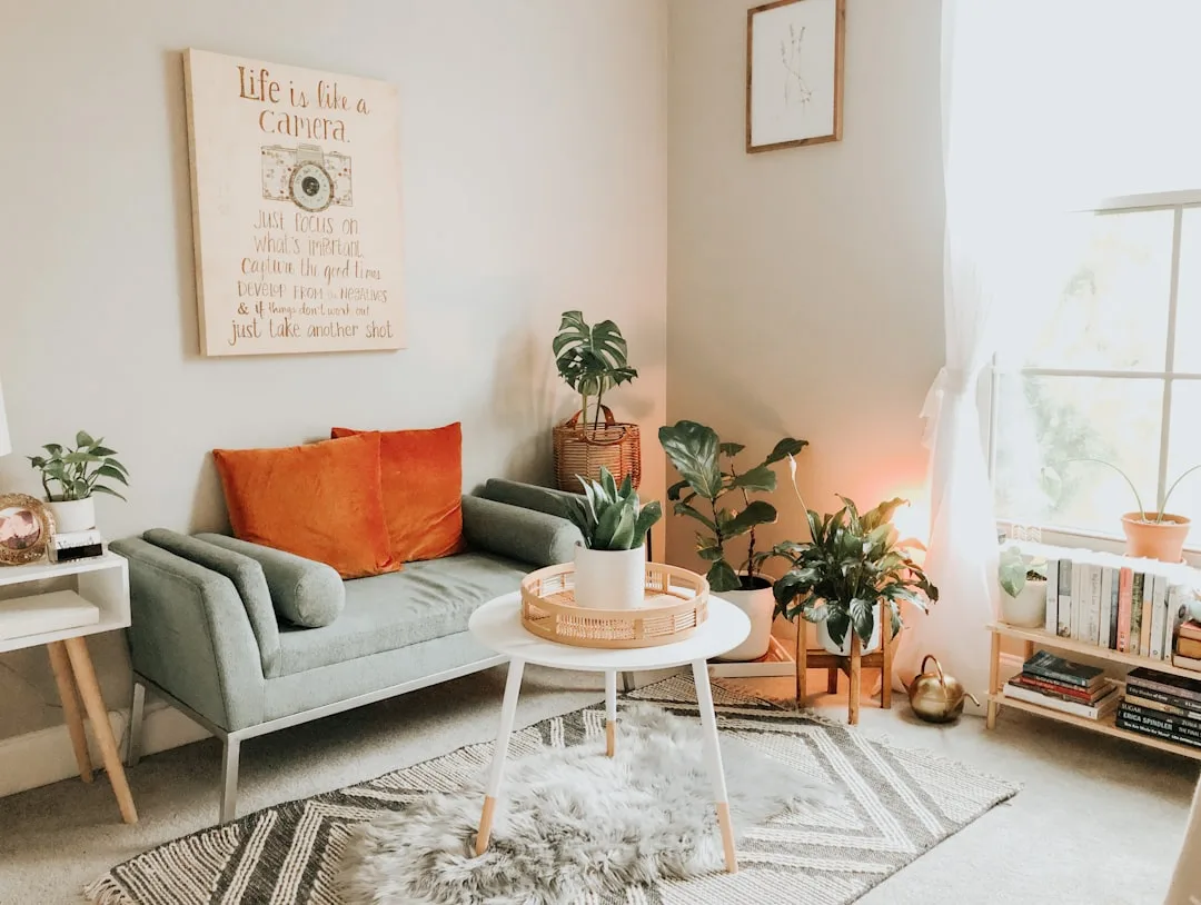 Cozy bohemian living room with gray sofa, orange pillows, houseplants, and inspirational wall art about life and cameras