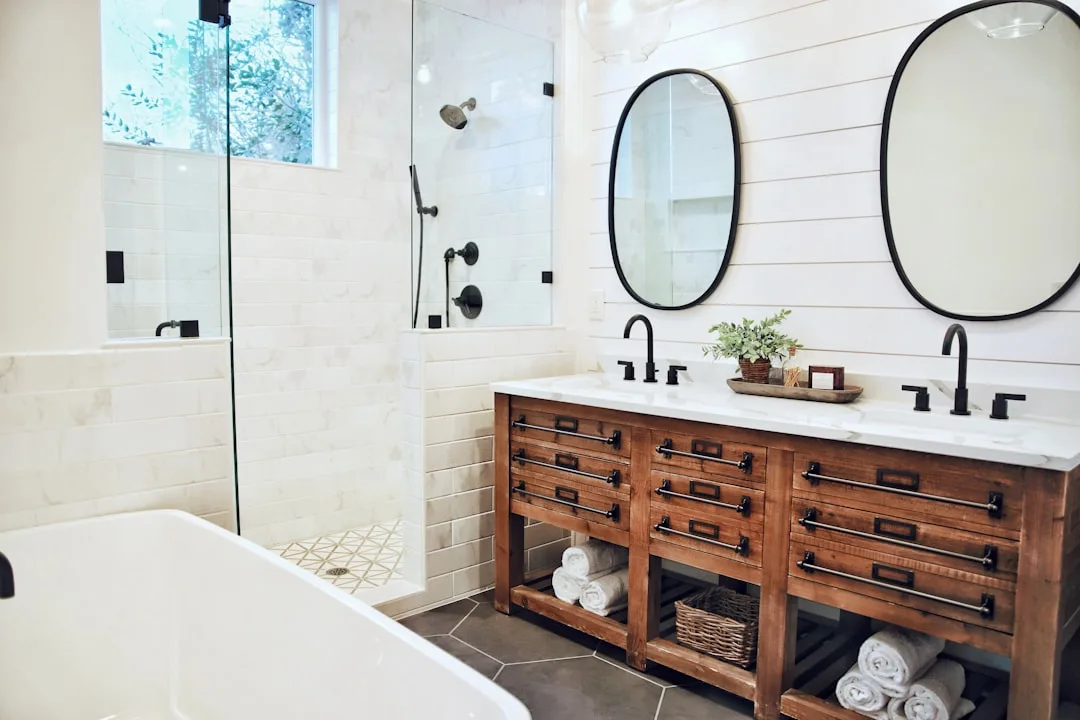 Farmhouse bathroom with rustic wood double vanity, open shelving with folded towels, and glass walk-in shower