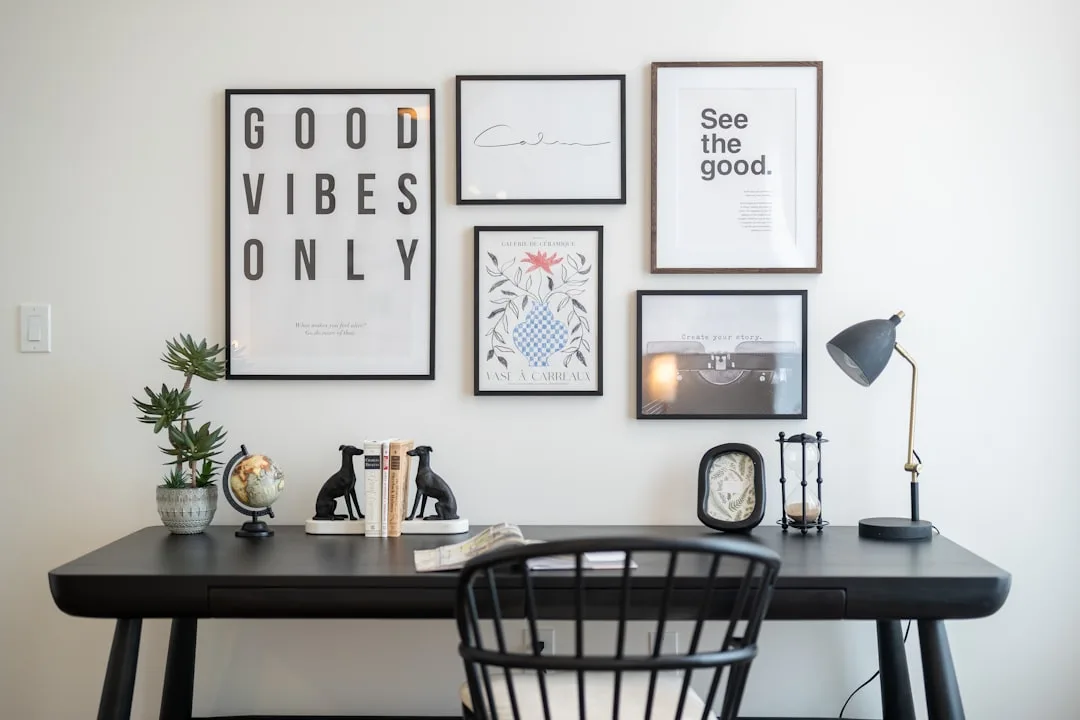 Minimalist black desk with gallery wall featuring motivational prints, bookends, globe, and desk lamp in home office
