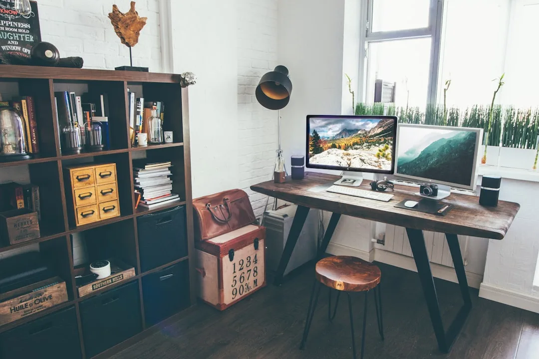 Rustic home office with bookshelf storage, wooden desk, dual monitors, and vintage trunk showing smart storage integrati