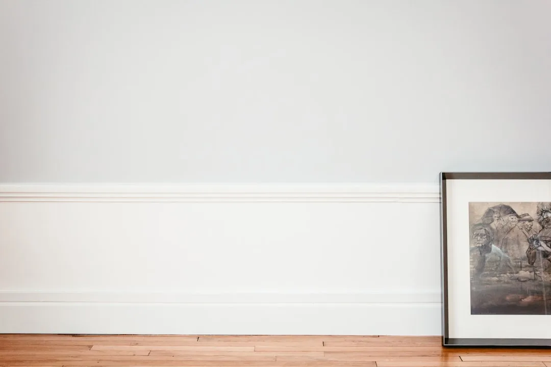 Framed artwork leaning against white baseboard wall on hardwood floor, showing affordable print framing idea