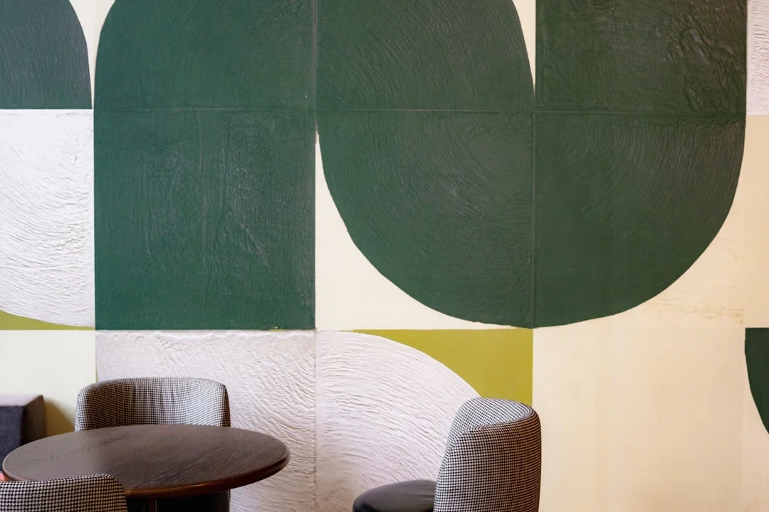 Houndstooth curved chairs with round table against geometric green mural wall in modern interior