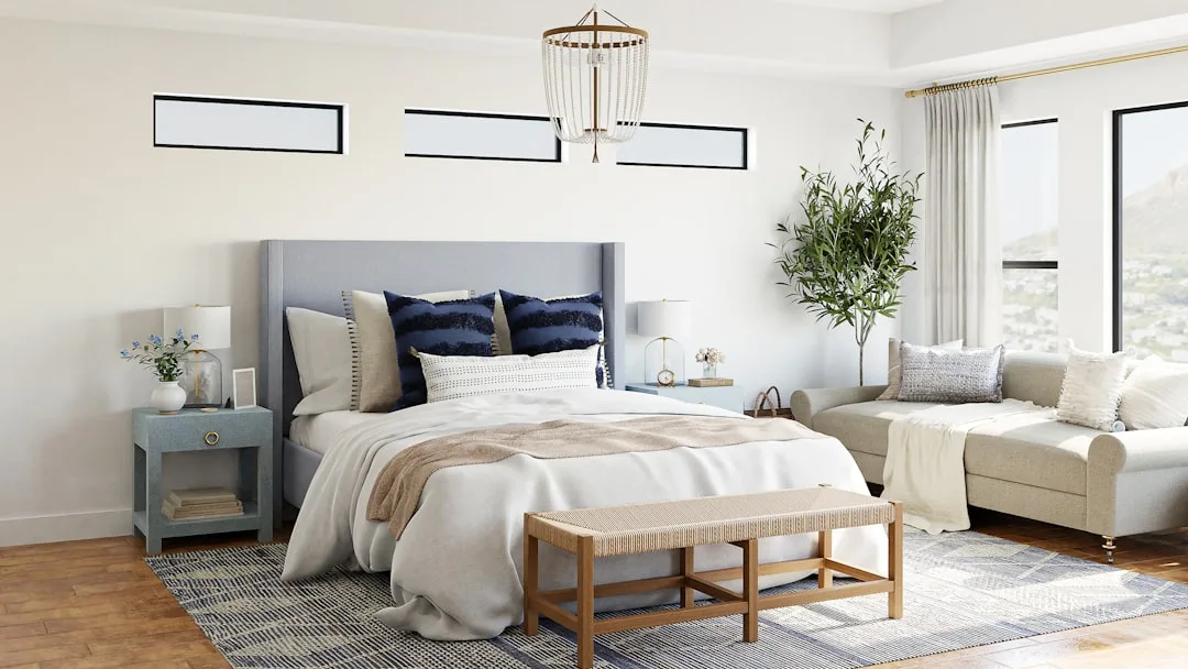 Neutral bedroom with gray upholstered headboard, navy accent pillows, beige throw, and layered textures on hardwood floo