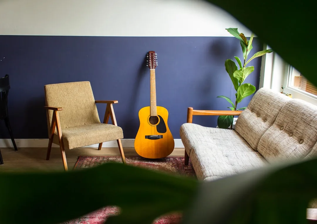 Acoustic guitar leaning against blue wall in mid-century modern living room with rug, armchair and sofa
